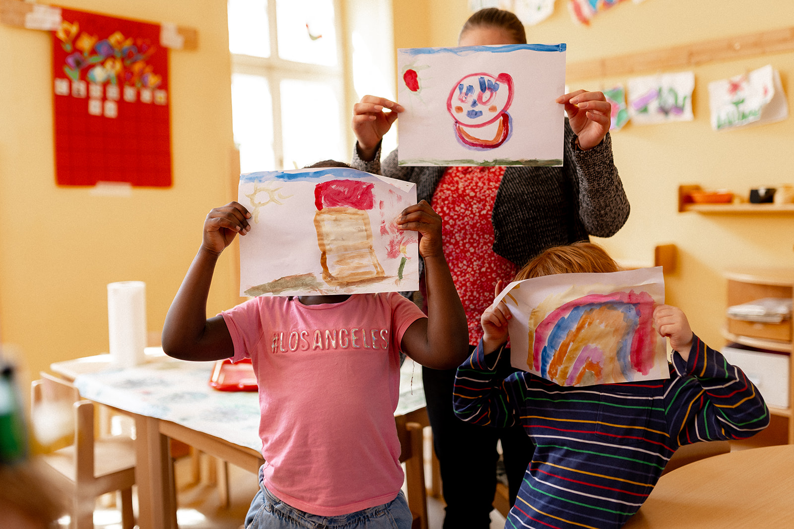 Kinder halten ihre selbst gemalten Bilder in den Händen.